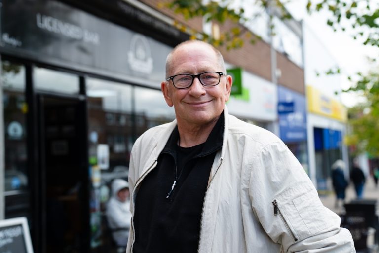 Man wearing glasses and a light jacket smiles.